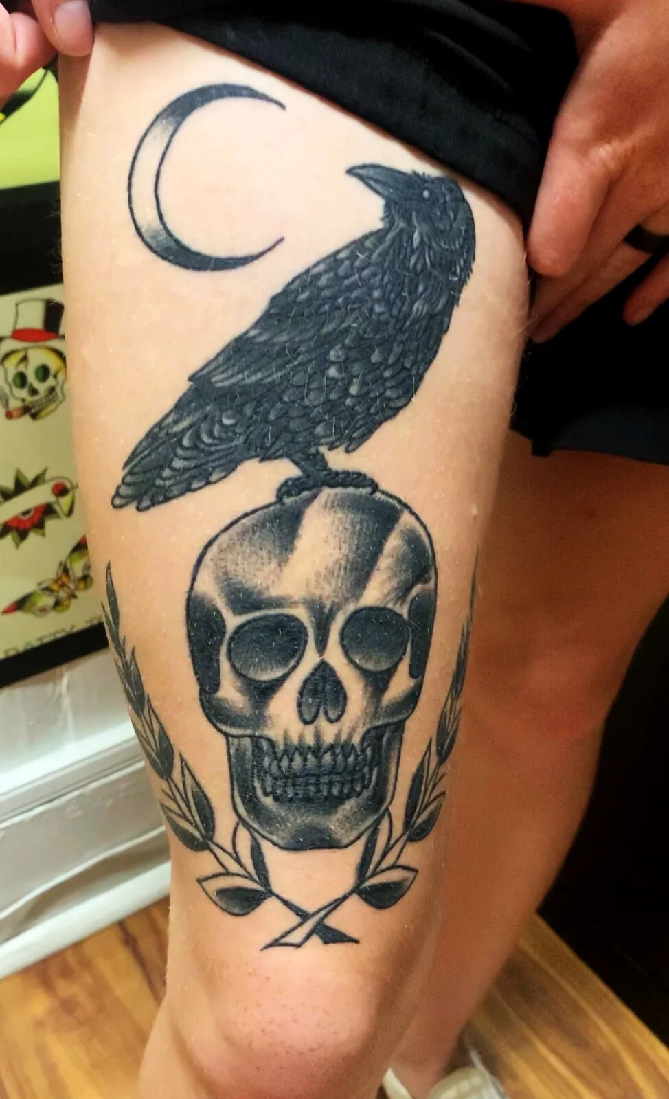 Black and grey traditional crow on skull with crescent moon and laurel wreath thigh tattoo by Tim Goodrich, Waikiki, Hawaii