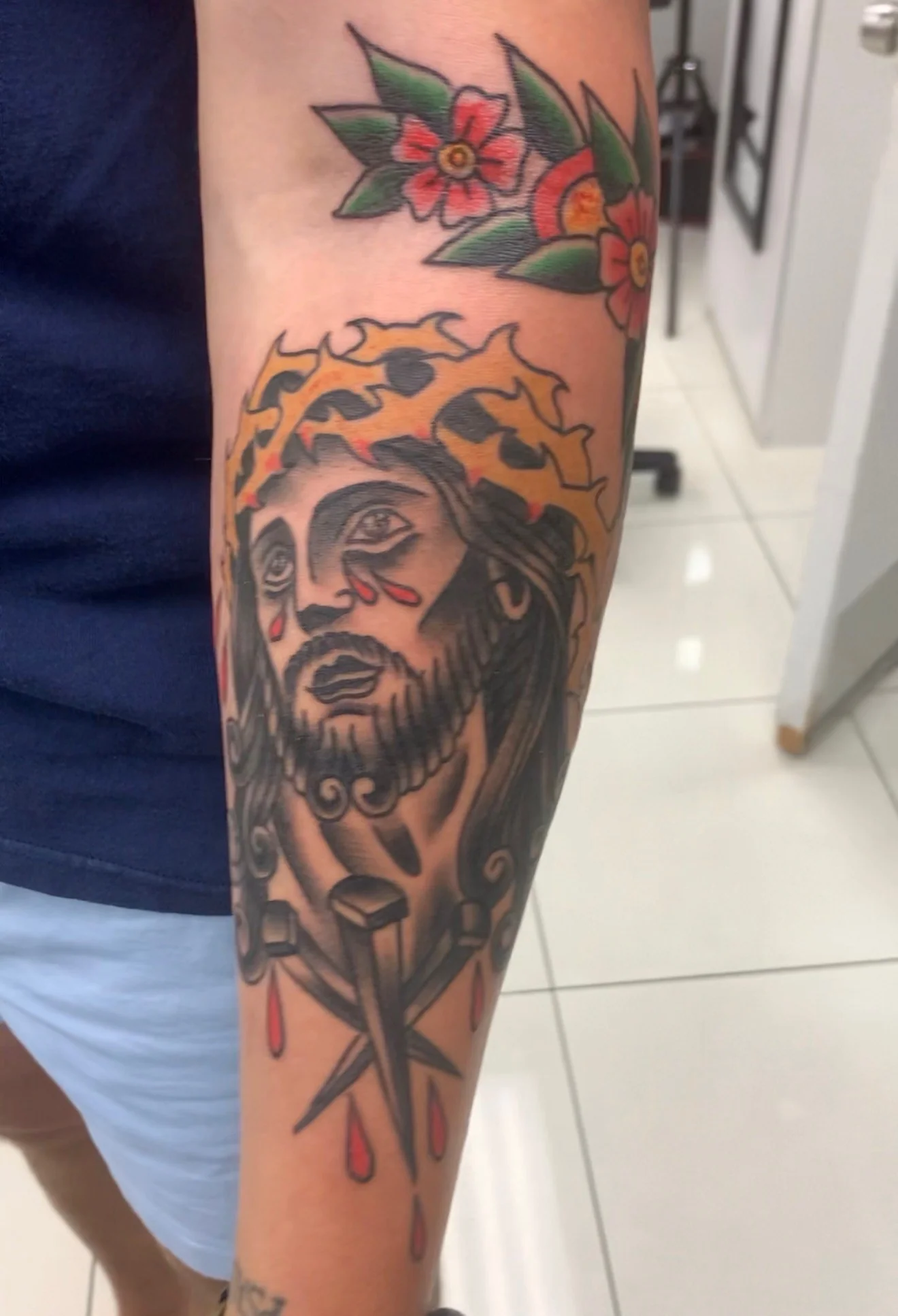American Traditional forearm tattoo of Christ in a crown of thorns weeping blood, with three iron nails and dripping blood drops below, by Tim Goodrich at his Waikiki tattoo shop, Hawaii.