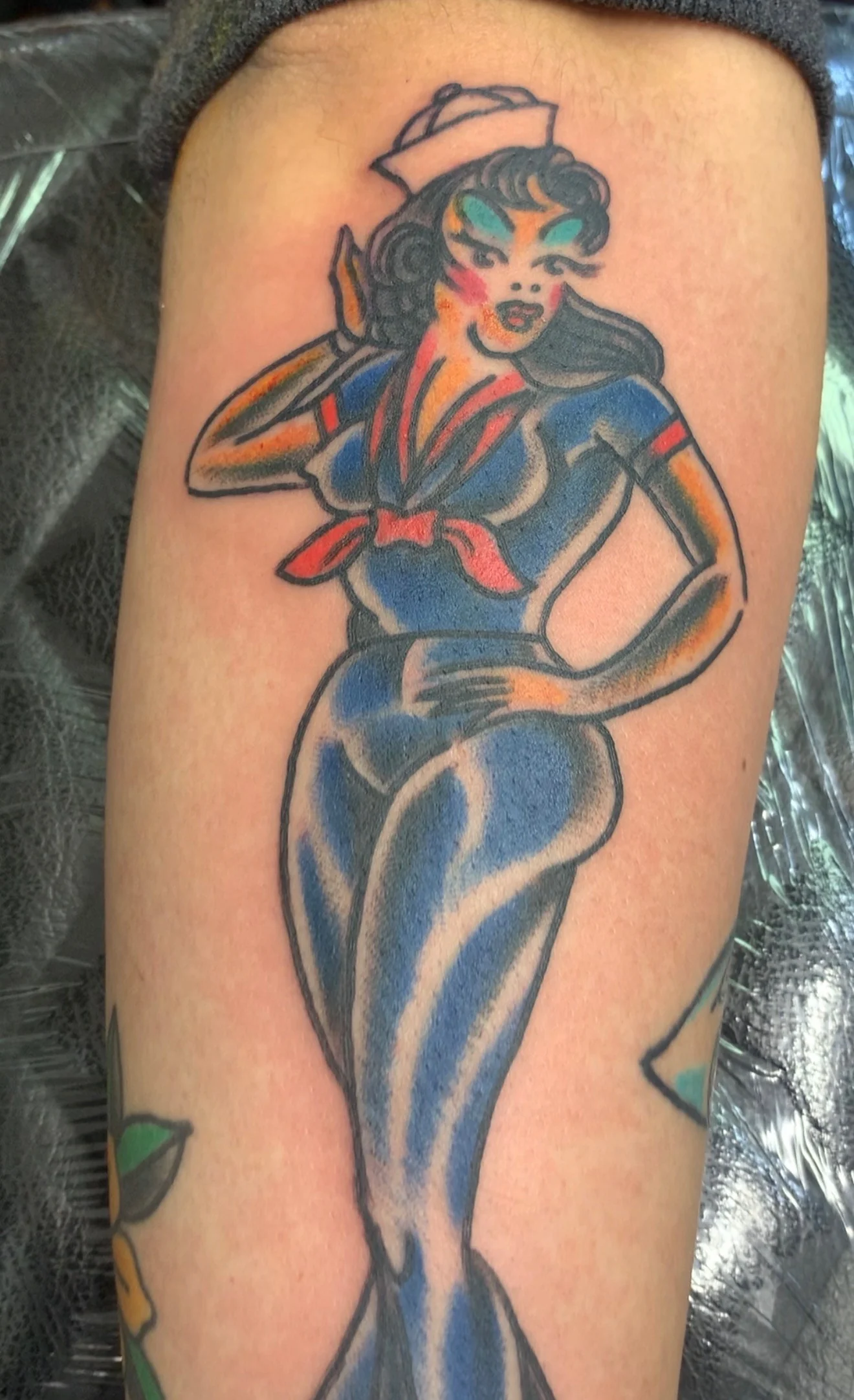American Traditional Sailor Jerry pin-up tattoo of a woman in blue sailor coveralls and white cap saluting, on the upper arm, by Tim Goodrich at his Waikiki tattoo shop, Hawaii.